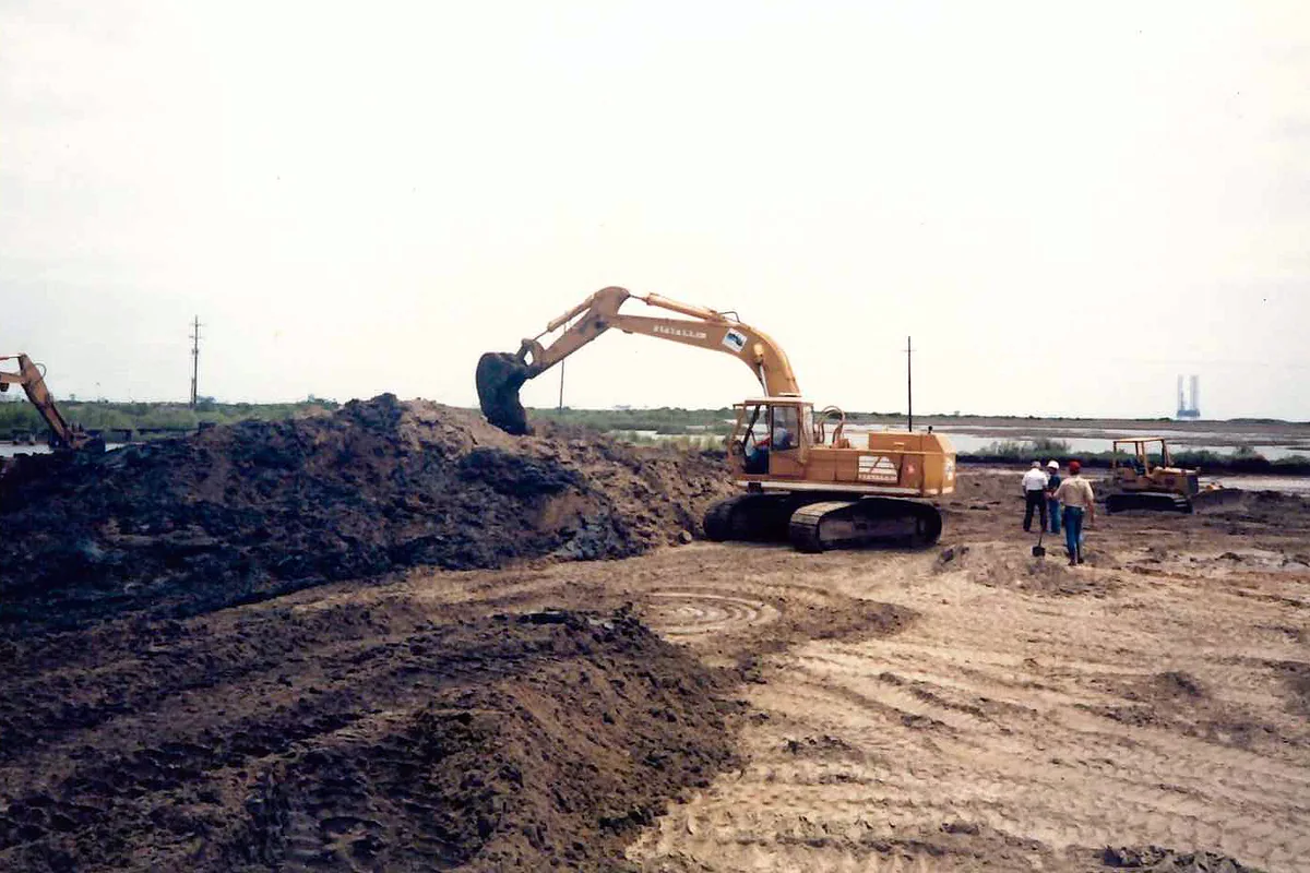 Excavator turning contaminated soil at a remediation site